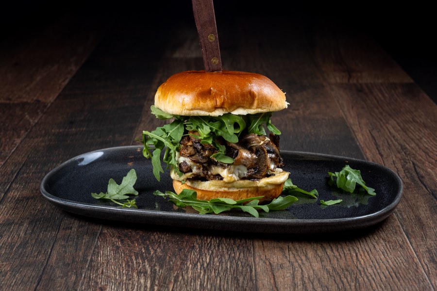 The Swiss Trifolati burger with mushrooms, melted Swiss cheese and arugula on a black plate, Ozys Tavern