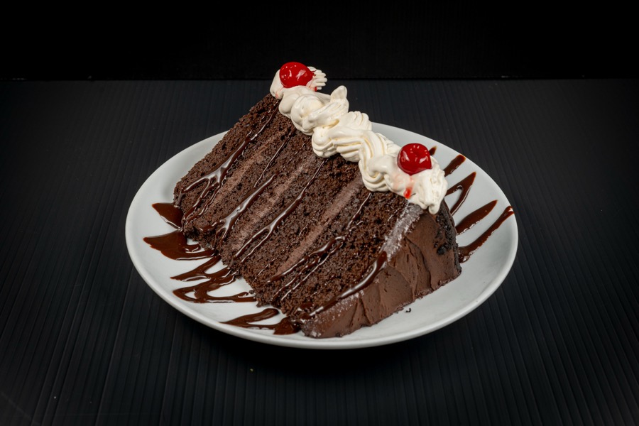Slice of chocolate layer cake with cream and a cherry