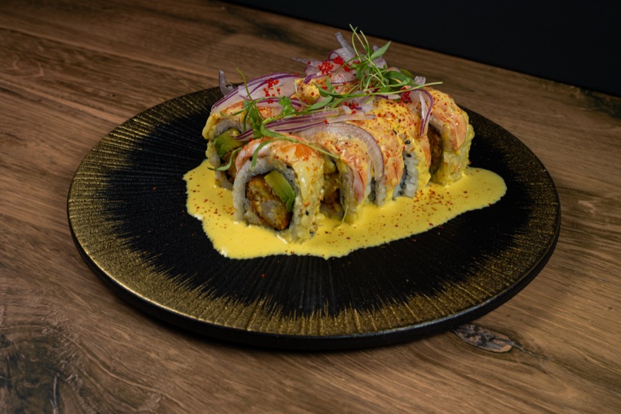 Sushi roll with yellow sauce on a black and gold plate