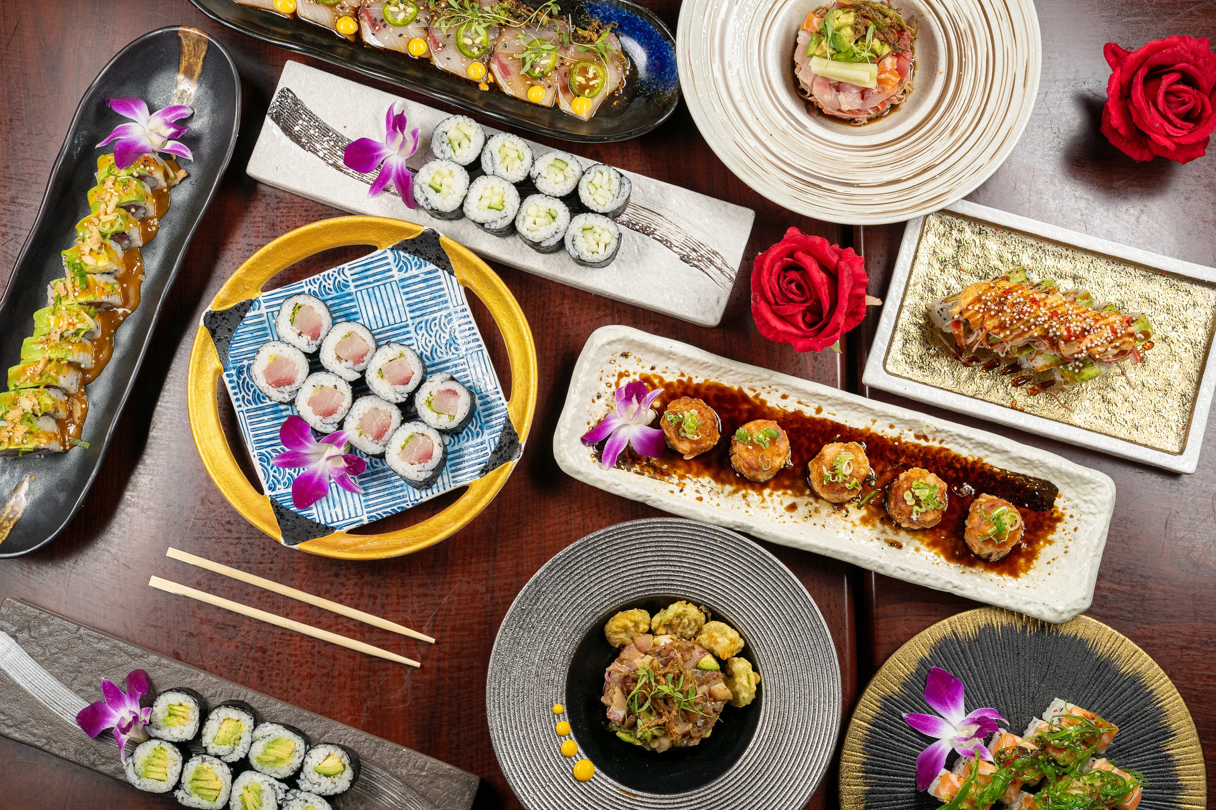 Table of sushi rolls, poke and small plates with orchids, seen from above