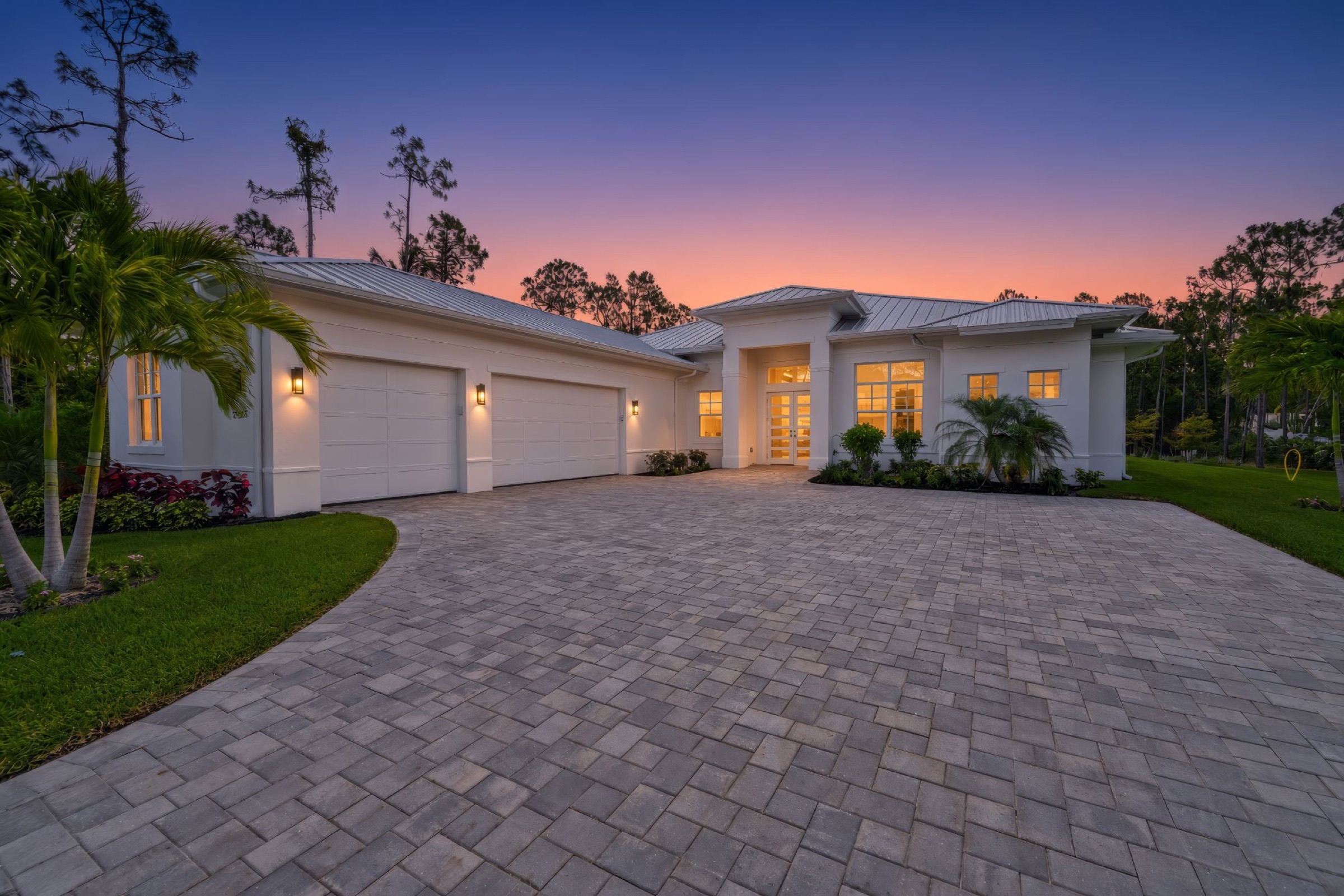White Florida home with a paver driveway at dusk, lights on